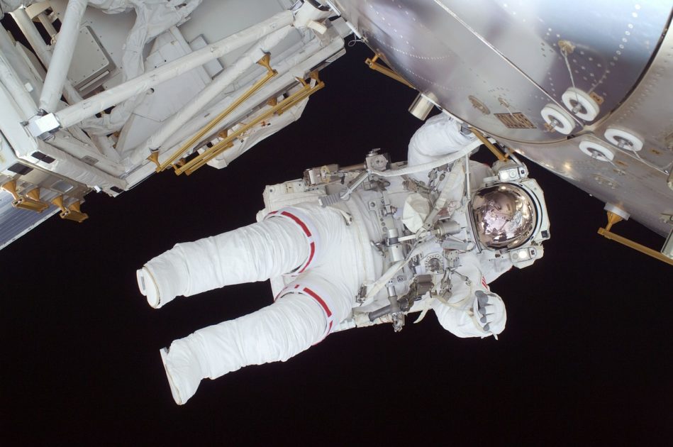 An Astronaut floating in space next to a space craft. The Astronaut is in a space suit and is almost horizontal