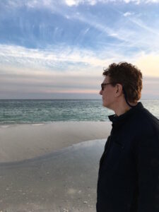 Photo of Richard Killian looking at the ocean, sea, water. Blue sky with some clouds. Richard Killian who worked at Penn State, Centre County Government, with background in internal controls. Richard Killian is a finance, accounting, budgeting, and financial reporting professional with more than 25 years of experience in university finance, nonprofit finance, county government, and public-sector financial operations. Photo taken at the beach outside in nature.