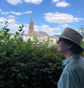 Photo of Richard Killian. He is looking to the river. A plant is in front of him with cityscape in the background. Richard Killian brings experience in sponsored programs financial analysis, budget reconciliation, accounts receivable monitoring, grant closeout support, and compliance-focused financial reporting. Photo location is Frankfurt Germany near the river walkway. 
